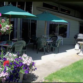 A sunny outdoor patio area with tables, chairs, and umbrellas, surrounded by colorful flowers.