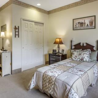 A cozy bedroom featuring a single bed with patterned bedding, a bedside table with a lamp, and wall art for decor.