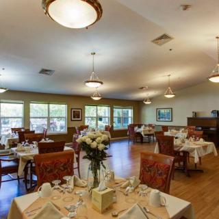 A spacious dining room with multiple tables set elegantly, featuring large windows and warm lighting.