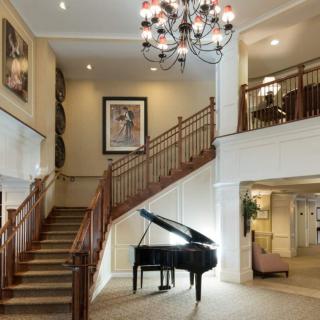 A luxurious lobby featuring a grand piano, elegant staircase, and chandelier.