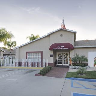 An office building entrance with an awning and adjacent parking lot, surrounded by palm trees.
