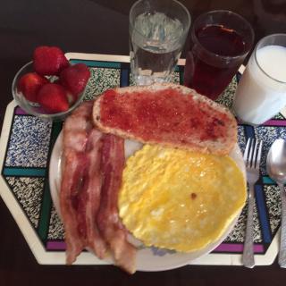 A hearty breakfast with bacon, eggs, toast with jam, strawberries, and drinks including milk, juice, and water.