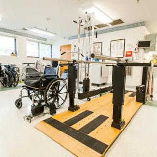 A rehabilitation room equipped with a wheelchair and parallel bars for physical therapy.