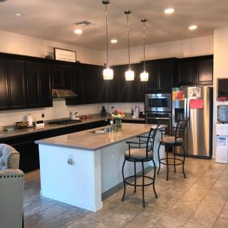 A modern kitchen with dark cabinets, an island with bar stools, and stainless steel appliances.