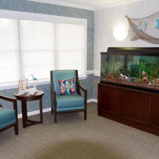 A cozy living room with an aquarium, two chairs, and a small table near the window.