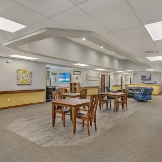 A spacious library interior with tables and chairs arranged on a carpeted floor.