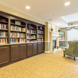 A cozy library room with bookshelves, a fireplace, and comfortable seating.