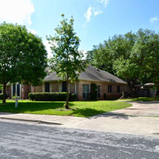 A suburban house with a green lawn and surrounding trees on a sunny day.