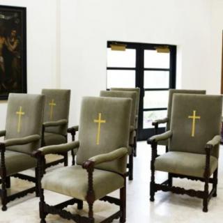 A room with upholstered chairs featuring embroidered crosses, likely a religious or church setting.