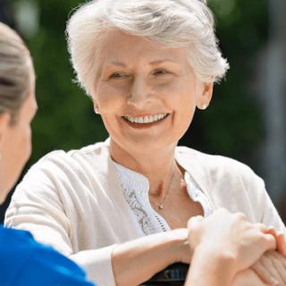 An elderly woman smiling while interacting with a caregiver outdoors.