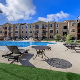 A beautiful apartment complex featuring a refreshing swimming pool and comfortable outdoor seating under a clear blue sky.