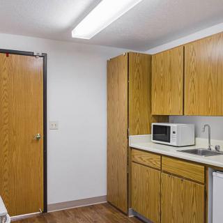 A small kitchenette with wooden cabinets, a microwave, and a sink.