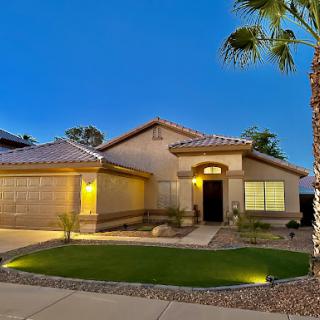 A beautifully illuminated residential home surrounded by well-maintained landscaping at dusk.