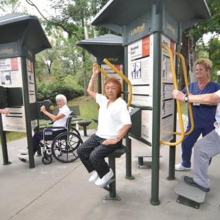 Seniors enjoying exercise at an outdoor gym in the park, with wheelchair-accessible equipment.