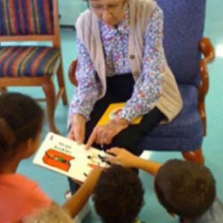 An elderly person reading a book to a group of children during storytime.