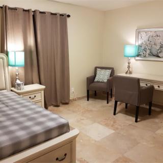 A cozy bedroom with a bed, desk, chair, and lamps.