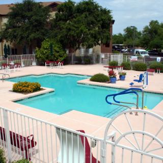 An outdoor swimming pool area with surrounding chairs and a fence under sunny skies.