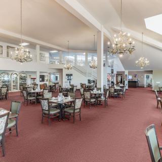 A spacious dining area with chandeliers, tables, and chairs on a carpeted floor.