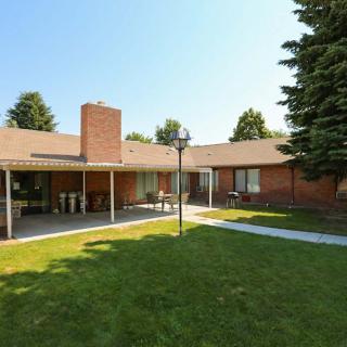 A spacious backyard with a lawn and patio area of a brick house, surrounded by trees.