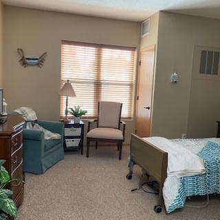 A cozy bedroom with a bed, chairs, and a window letting in natural light.
