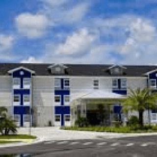 A modern blue and white hotel building with palm trees under a partly cloudy sky.