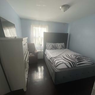 A small, cozy bedroom with a bed, dresser, chair, and a window letting in natural light.