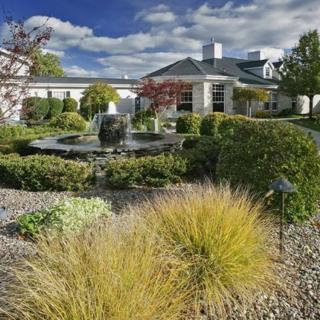 A scenic view of a landscaped garden with a central fountain, surrounded by a modern building and clear blue sky.