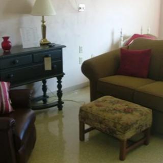 A cozy living room setup with a sofa, armchair, ottoman, and a side table with a lamp.