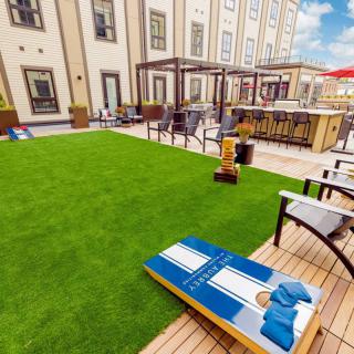 A rooftop lounge with a grass lawn, seating area, and cornhole game on a sunny day.