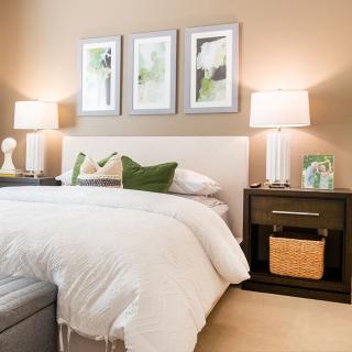 A cozy bedroom with elegant decor, featuring a bed with white bedding, two side tables with lamps, and three framed pictures on the wall.