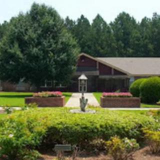 A landscaped garden with a pathway leading to a fountain and a house surrounded by trees.
