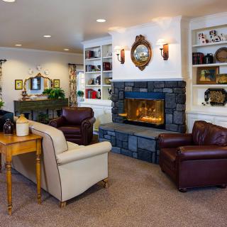 A cozy living room with a stone fireplace, comfortable seating, and decorative shelves.