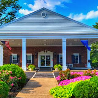 A charming building with a welcoming entrance surrounded by vibrant flowers and a clear blue sky.
