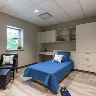 A modern and minimalist single bedroom with blue bedding, featuring built-in storage and natural lighting.