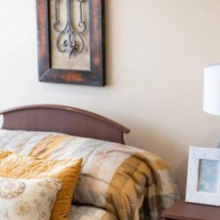 A cozy bedroom featuring a bed with plaid bedding, decorative pillows, a bedside lamp, and a wall hanging.
