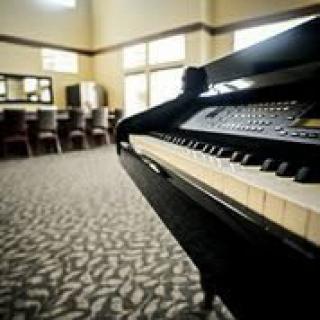 A piano in a well-lit music room with chairs and large windows.