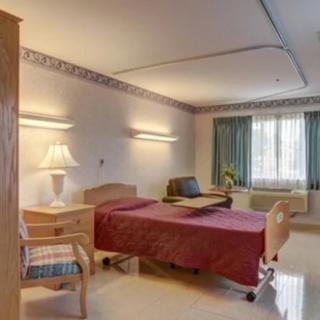 A clean and neatly arranged hospital room with a single bed, a lamp, and a window with curtains.