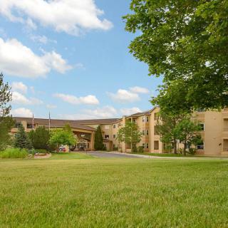 A hotel building surrounded by green grass and trees under a blue sky with clouds.