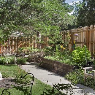 A serene backyard garden featuring lush greenery, a wooden fence, and a paved pathway.