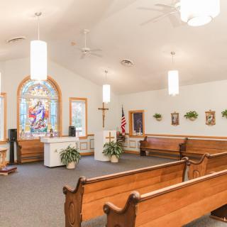 Interior view of a church showing pews, stained glass, and the altar.