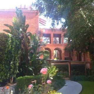 A beautiful view of a brick building surrounded by lush greenery and blooming flowers.