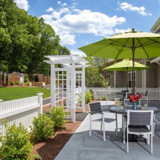 A sunny outdoor patio with a white fence, green umbrellas, and garden seating.