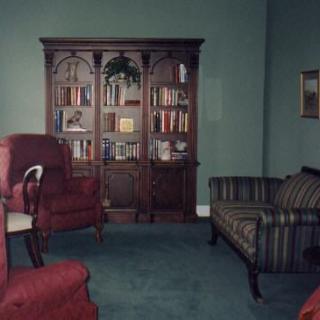 A traditional living room with a large bookshelf, upholstered chairs, and green walls.