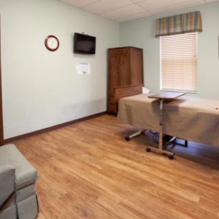 A hospital room with a bed, TV, and clock on the wall.
