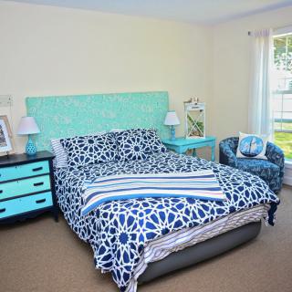 A cozy bedroom with a blue and white color scheme, featuring a bed with patterned bedding, matching furniture, and natural light streaming in through the window.