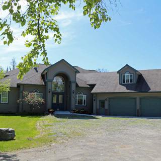 A spacious suburban house with a three-car garage, surrounded by greenery on a sunny day.