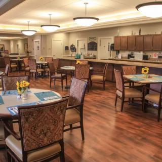 A well-lit dining area with multiple tables and chairs arranged on wooden flooring.