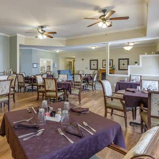 A well-lit dining room with neatly arranged tables and chairs, featuring ceiling fans and subtle decor.