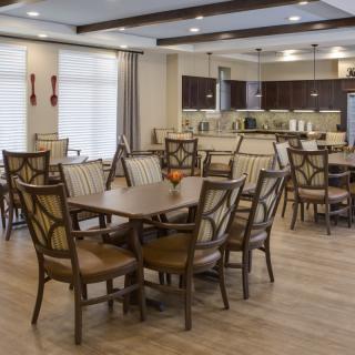 A modern dining room with multiple tables and chairs, featuring a kitchen area in the background.