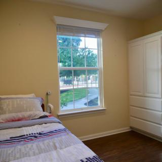 A bright and simple bedroom with a single bed, window, and white wardrobe.